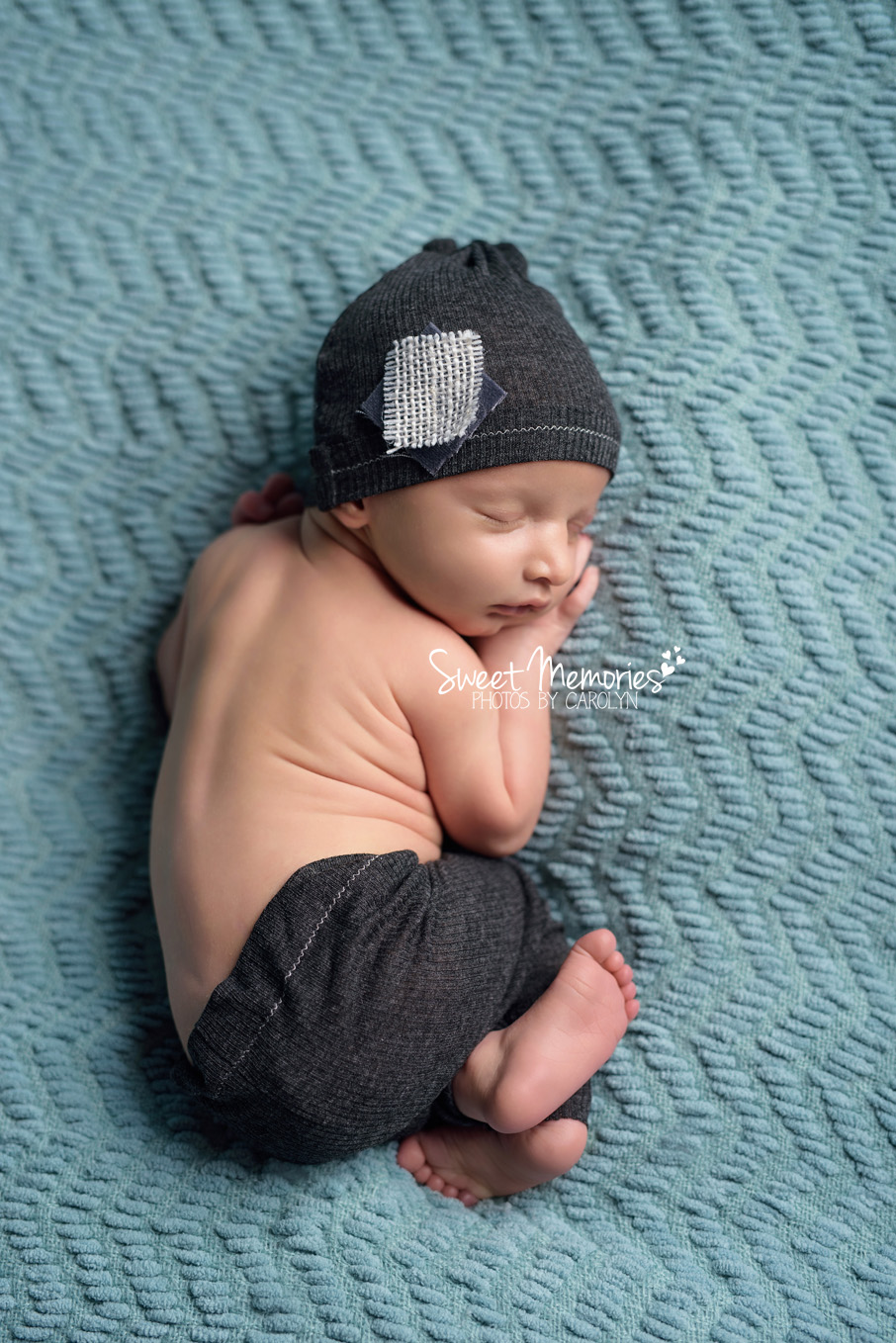 newborn boy in pants and hat on teal
