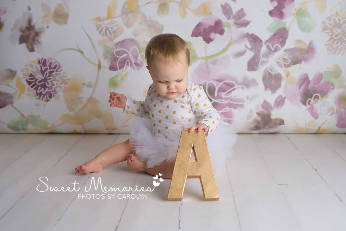 Purple and gold floral backdrop with one year old girl in a tutu holding the letter A in Quakertown, PA | Sweet Memories Photos by Carolyn