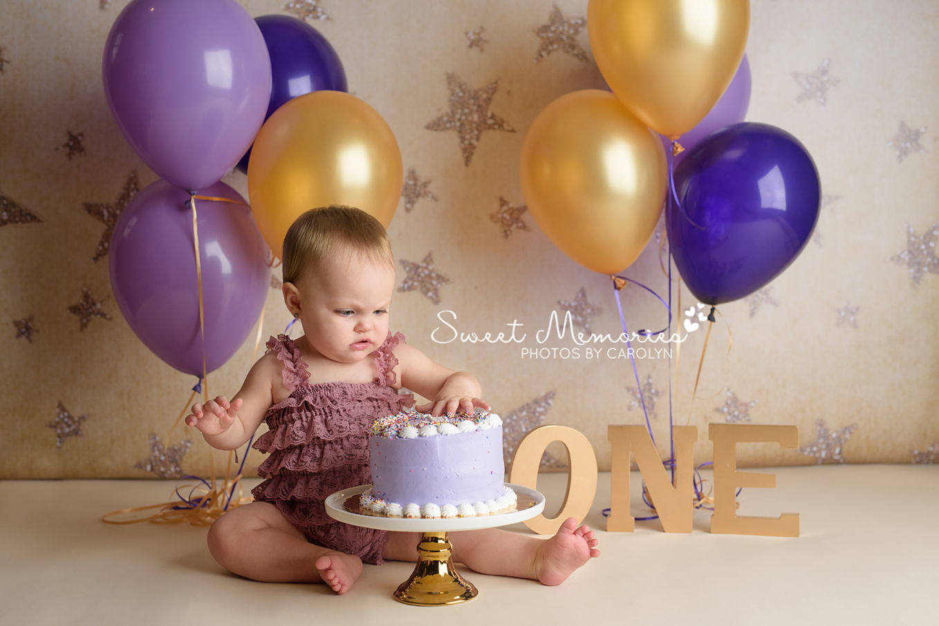 One year old girl in lace romper with purple cake on gold star background with gold and purple balloons | Sweet Memories Photos by Carolyn