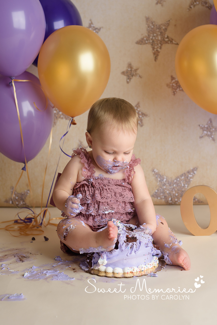 one year old girl cake smash with foot in cake on gold star backdrop and purple and gold balloons in Quakertown | Sweet Memories Photos by Carolyn