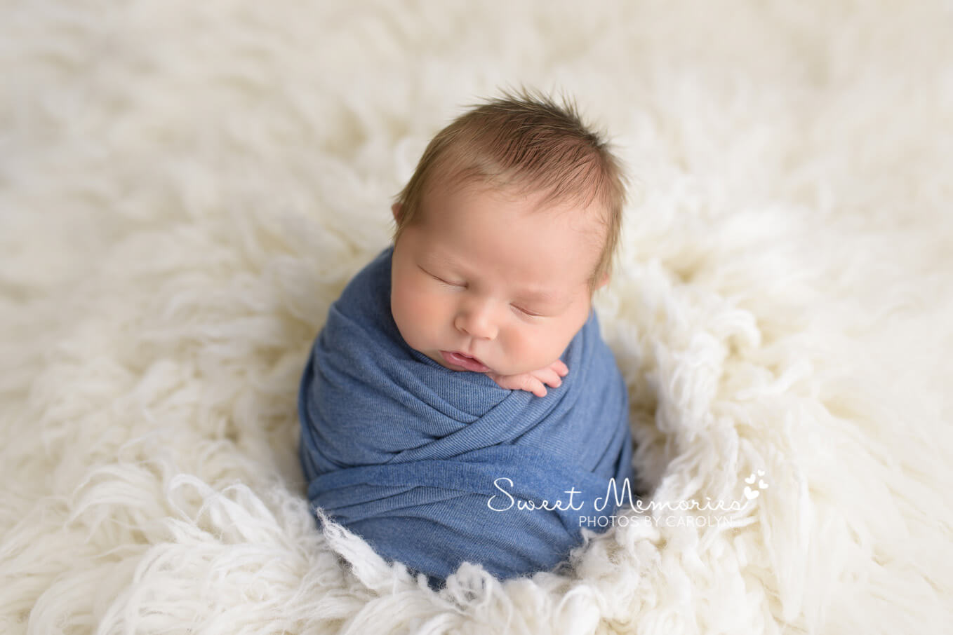 newborn sleeping wrapped in blue on white fur blanket