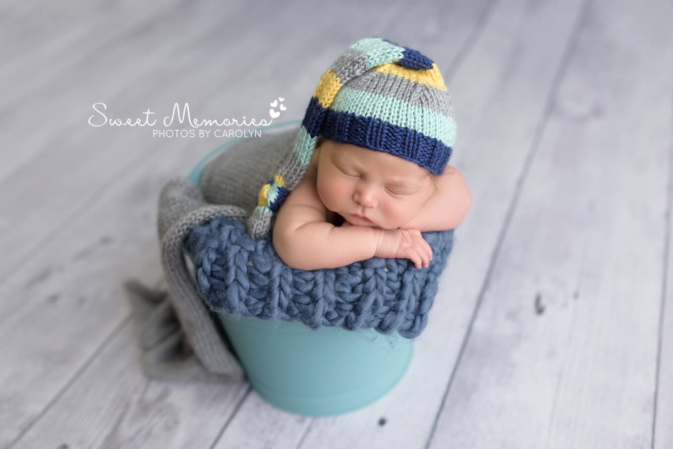 baby boy wearing blue and gray striped hat in chin on hands bucket pose