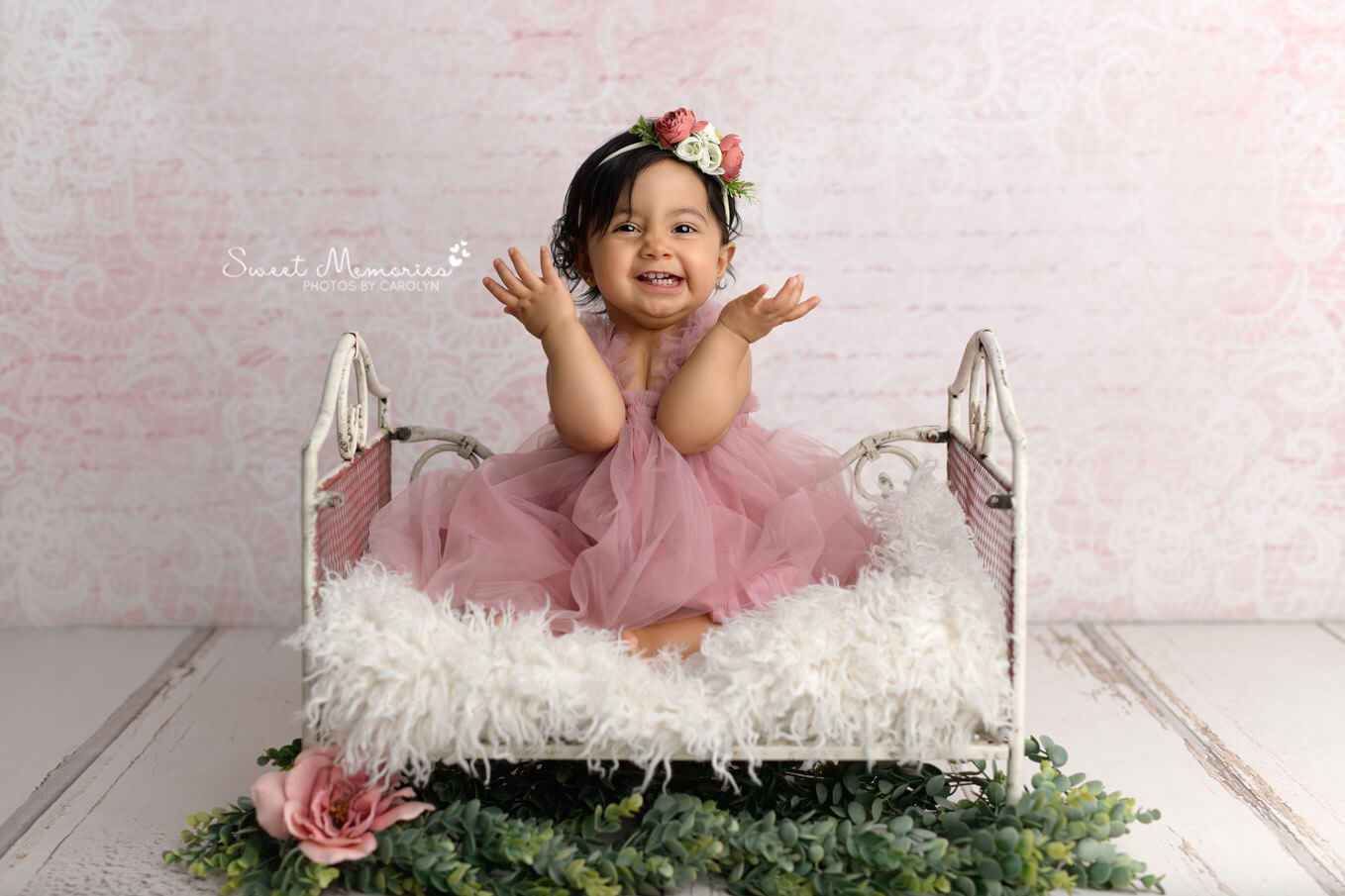 Smiling baby girl with hands up sitting on bed prop with pink backdrop | Austin cake smash photography